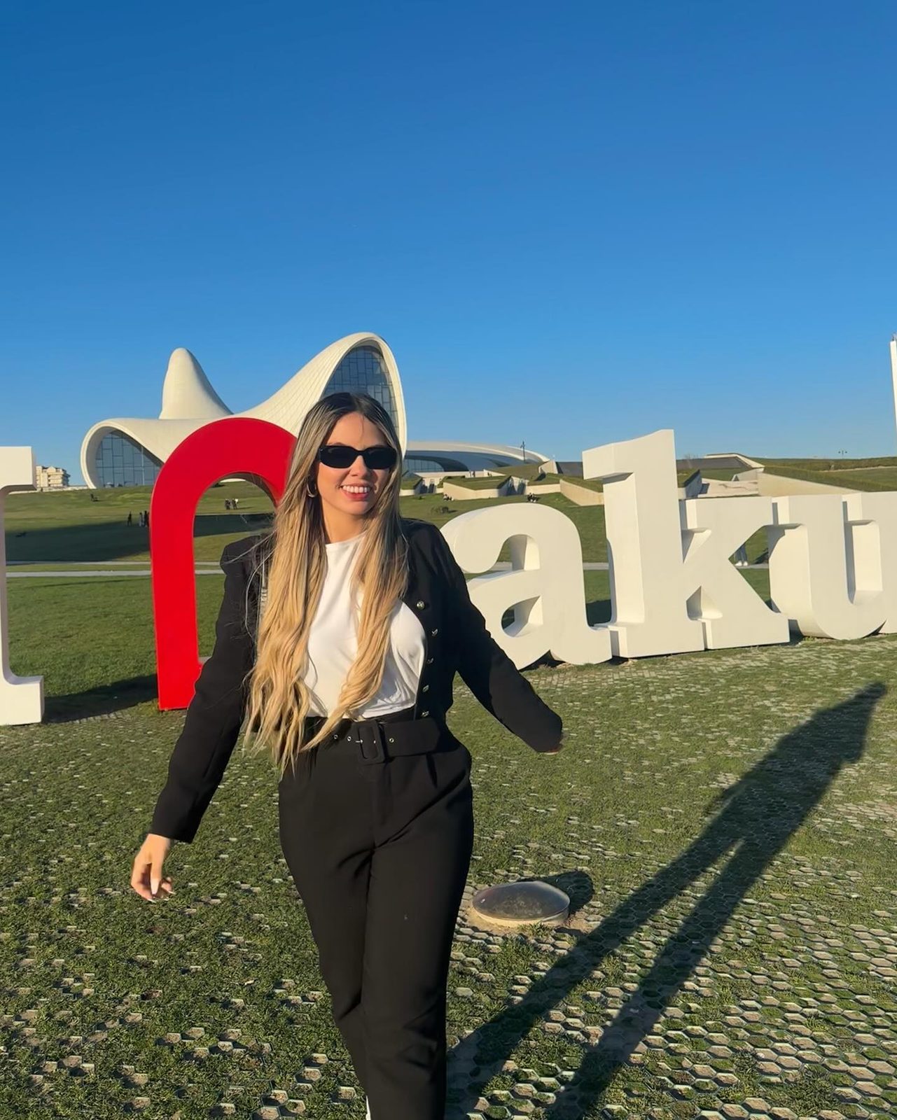 Isabella Duarte in a black suit and white shirt by the Baku sign